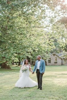 a bride and groom holding hands walking through the grass