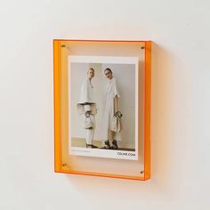 an orange frame holds two photos of men in white coats and shoes, one is holding a handbag