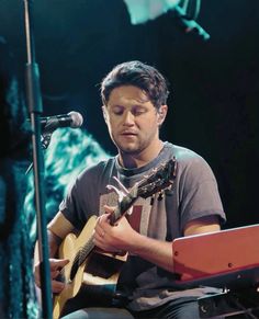 a man sitting in front of a microphone playing a guitar