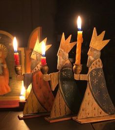 three wooden figurines with lit candles in them