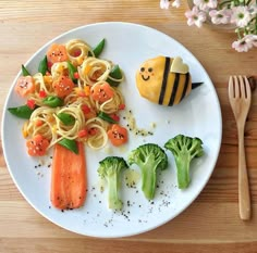 a white plate topped with pasta and veggies next to a bee shaped toy