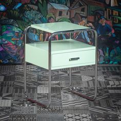 a green table with a drawer on it in front of a colorful wall and floor