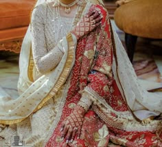 a woman in a red and gold bridal dress sitting on the floor with her hands clasped to her chest