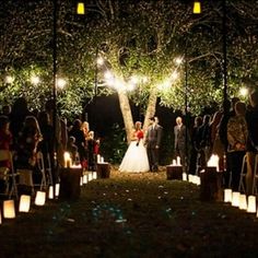 a bride and groom are walking down the aisle at their outdoor wedding ceremony with candles lit up in front of them