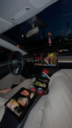 a person in a car with food and drinks on the tray while watching tv at night