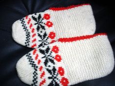 two white knitted mittens with red and black designs on them sitting next to each other