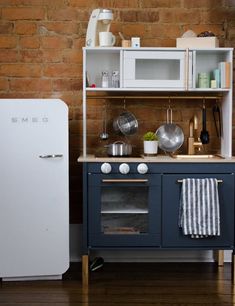 a small kitchen with an old fashioned stove and refrigerator in front of a brick wall