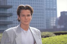 a young man in a suit and tie posing for the camera with tall buildings behind him