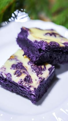 two pieces of purple cake sitting on top of a white plate next to green leaves