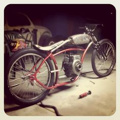 a red and black motorcycle sitting on top of a garage floor next to a car