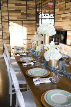 the table is set with white flowers and gold vases on it's sides