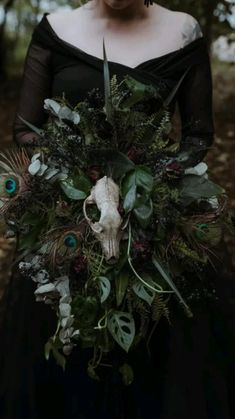 a woman in a black dress holding a bouquet with feathers and flowers on it's side