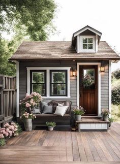 a small gray and white house with flowers on the front porch, sitting area next to it