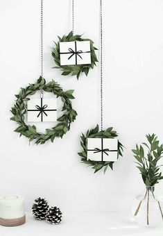 three ornaments are hanging on the wall and decorated with greenery, pine cones and bows