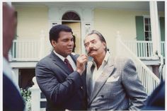 two men standing in front of a house one is fixing the other's tie