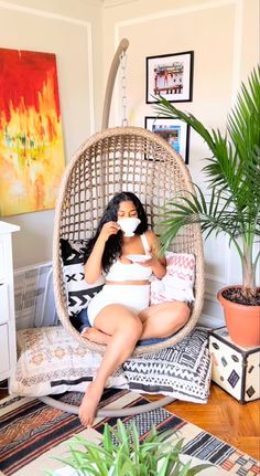 a woman sitting in a hanging chair with a mask on her face while holding a cup