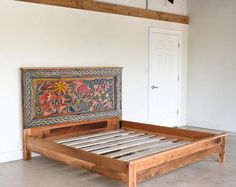 a wooden bed frame with intricate designs on the side and foot board, in an empty room