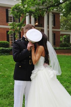 a bride and groom kissing in front of a large brick building on their wedding day