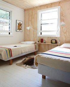 two beds in a small room with wood paneling on the walls and windows above them