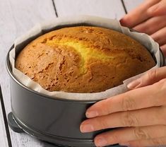 a person holding a loaf of bread in a pan on top of a wooden table