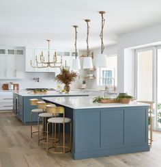 a kitchen with blue cabinets and white counter tops, gold stools and chandeliers