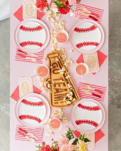 an overhead view of a baseball themed table setting with pink and red flowers, plates, napkins and utensils