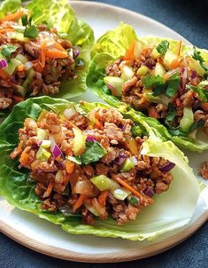 three lettuce cups filled with meat and vegetables on a white plate, ready to be eaten