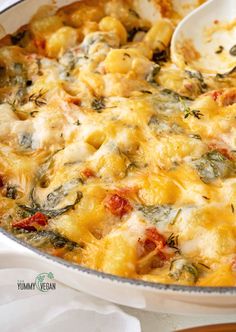 a casserole dish with spinach, cheese and tomatoes is being spooned