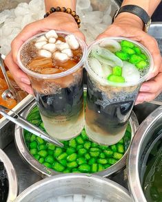 two people are holding cups with drinks in them and some ice cubes on the side