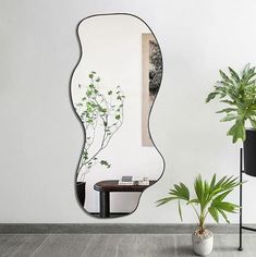 a mirror sitting next to a potted plant on top of a wooden table in front of a white wall