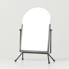 a mirror sitting on top of a metal stand next to a white wall and floor