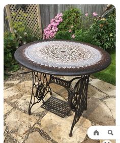 an old sewing machine table is sitting on a patio with pink flowers in the background