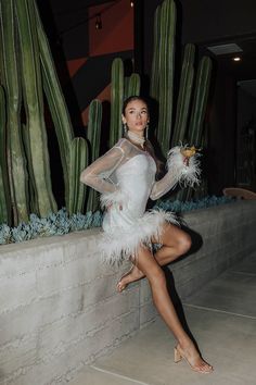 a woman in a white dress posing next to a cactus