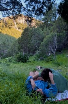 two people are laying in the grass with their backs to each other and one is covering his face