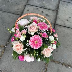 a basket filled with pink and white flowers sitting on top of a brick floor next to a sidewalk