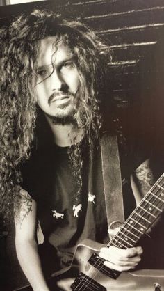 a black and white photo of a man with long hair holding a guitar in his hands