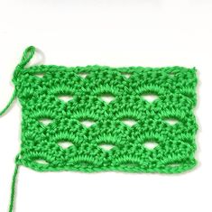 a green crochet square with a knot on the end and two holes in the middle