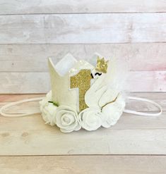 a white crown with gold glitter number one on it sitting on a wooden floor next to flowers