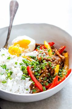 a white bowl filled with rice, meat and veggies next to a fork