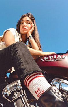 a woman sitting on top of a motorcycle with her feet propped up against the seat