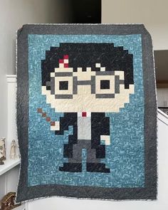 an image of a person holding up a pixel art quilt in the shape of harry potter