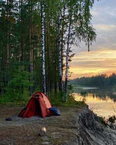 a red tent sitting on top of a lush green forest next to a body of water