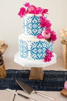 a blue and white wedding cake with pink flowers on top, sitting on a table