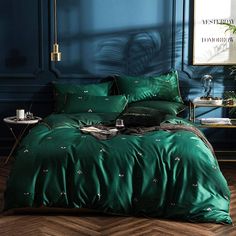 a bed with green comforter and pillows in a room next to a blue wall