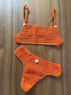 two pieces of orange crochet swimsuit on a wooden surface