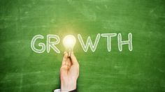 the word growth written on a chalkboard with a hand holding a lightbulb