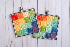 two colorful patchwork coasters sitting on top of a white wooden table next to each other