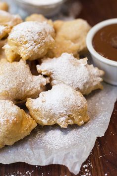 powdered sugar covered pastries and dipping sauce on a wooden table with napkins