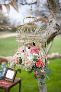 a birdcage filled with flowers hanging from a tree