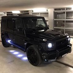 a black mercedes g - class is parked in a parking garage with its lights on